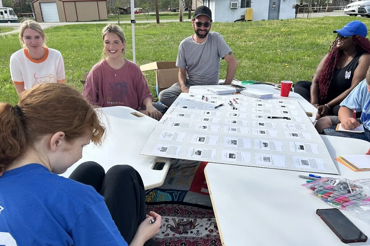 A group of students sits outside discussing and building a foldable poster board for the AJRC